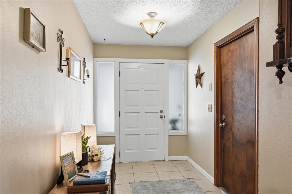An entryway features a white front door with sidelights, tile flooring, and a wooden console table — 3028 WOOD SONG COURT, MULBERRY, FL