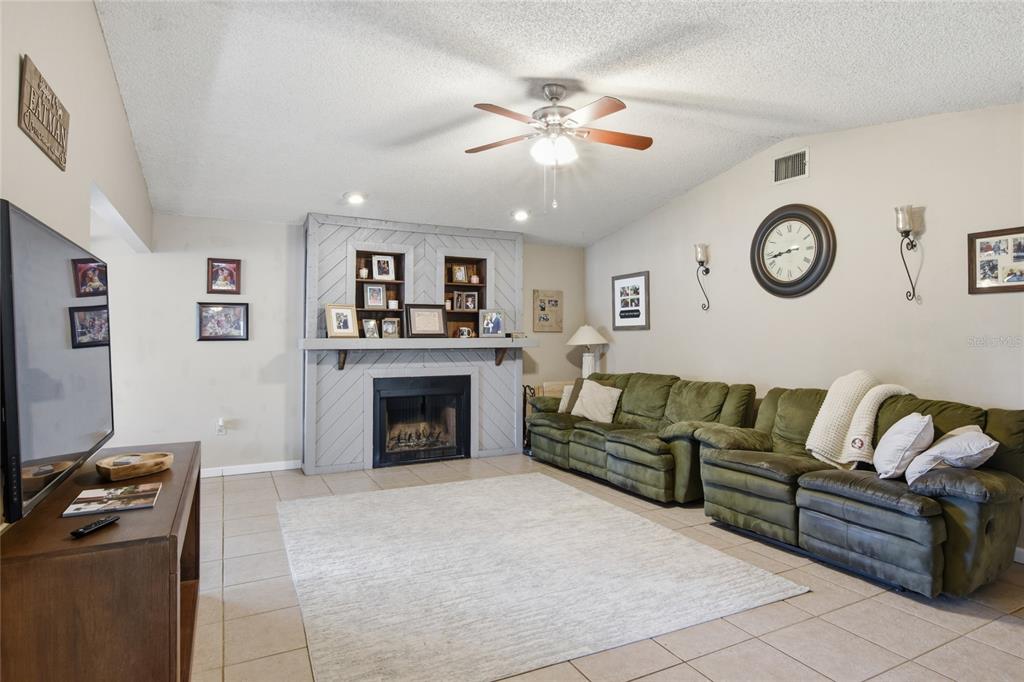 A living room features a gray fireplace, a green sectional sofa, and a ceiling fan — 3028 WOOD SONG COURT, MULBERRY, FL