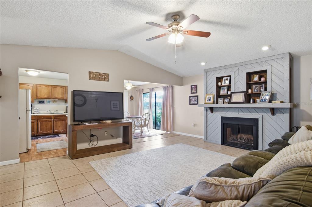 A living room features a fireplace with a gray herringbone surround, tile flooring, and a ceiling fan — 3028 WOOD SONG COURT, MULBERRY, FL