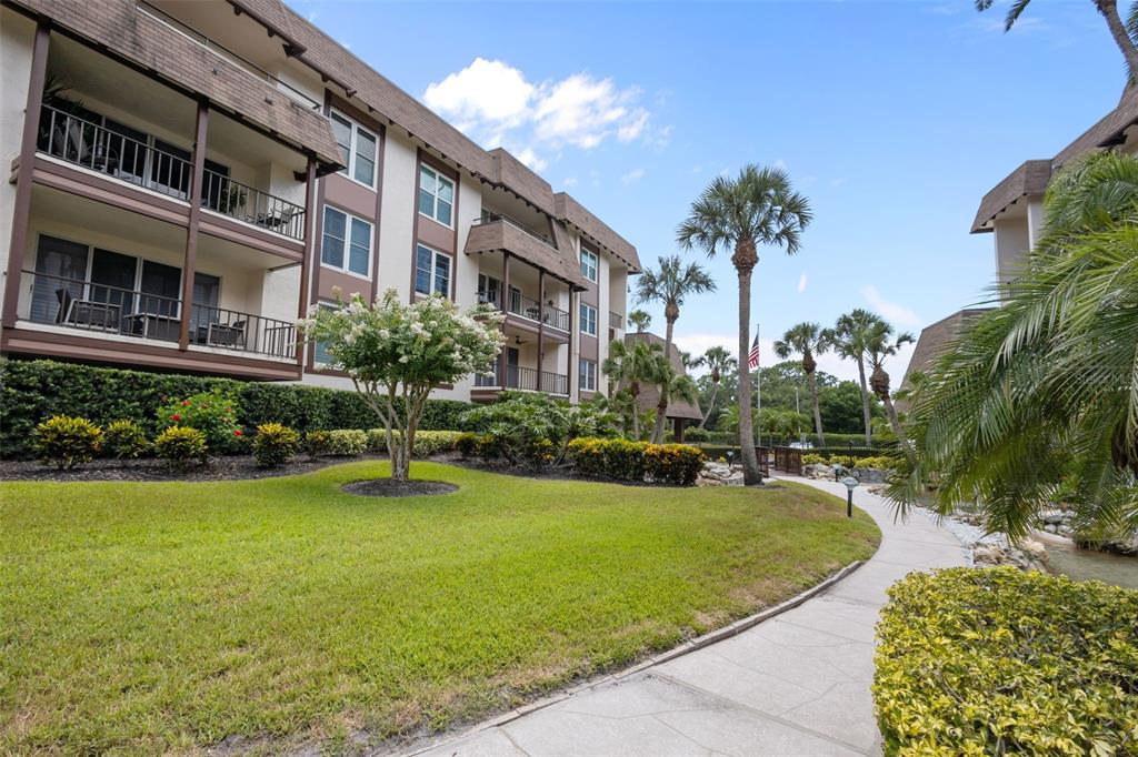 A multi-story apartment building features balconies overlooking a landscaped lawn and a paved walkway — 3021 COUNTRYSIDE BOULEVARD UNIT 21A, CLEARWATER, FL