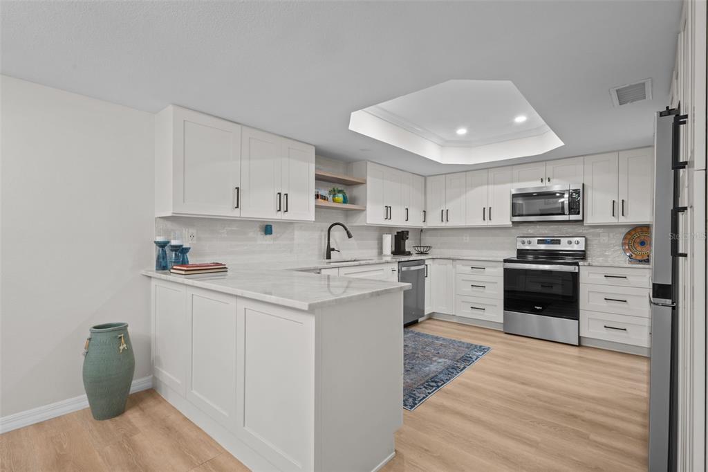 A modern kitchen features white cabinetry, stainless steel appliances, and a marble-topped peninsula — 3021 COUNTRYSIDE BOULEVARD UNIT 21A, CLEARWATER, FL