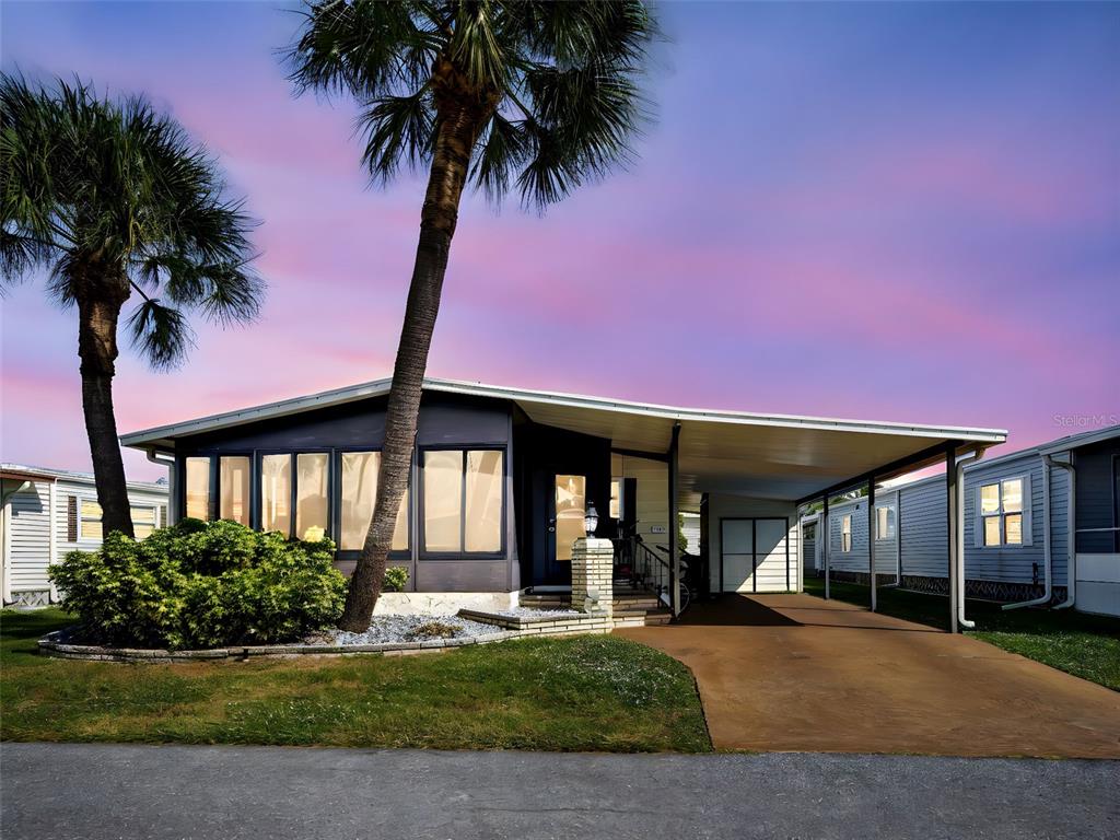 A single-story mobile home features a dark exterior, a carport, and two palm trees — 2100 KINGS HIGHWAY UNIT 1067, PORT CHARLOTTE, FL