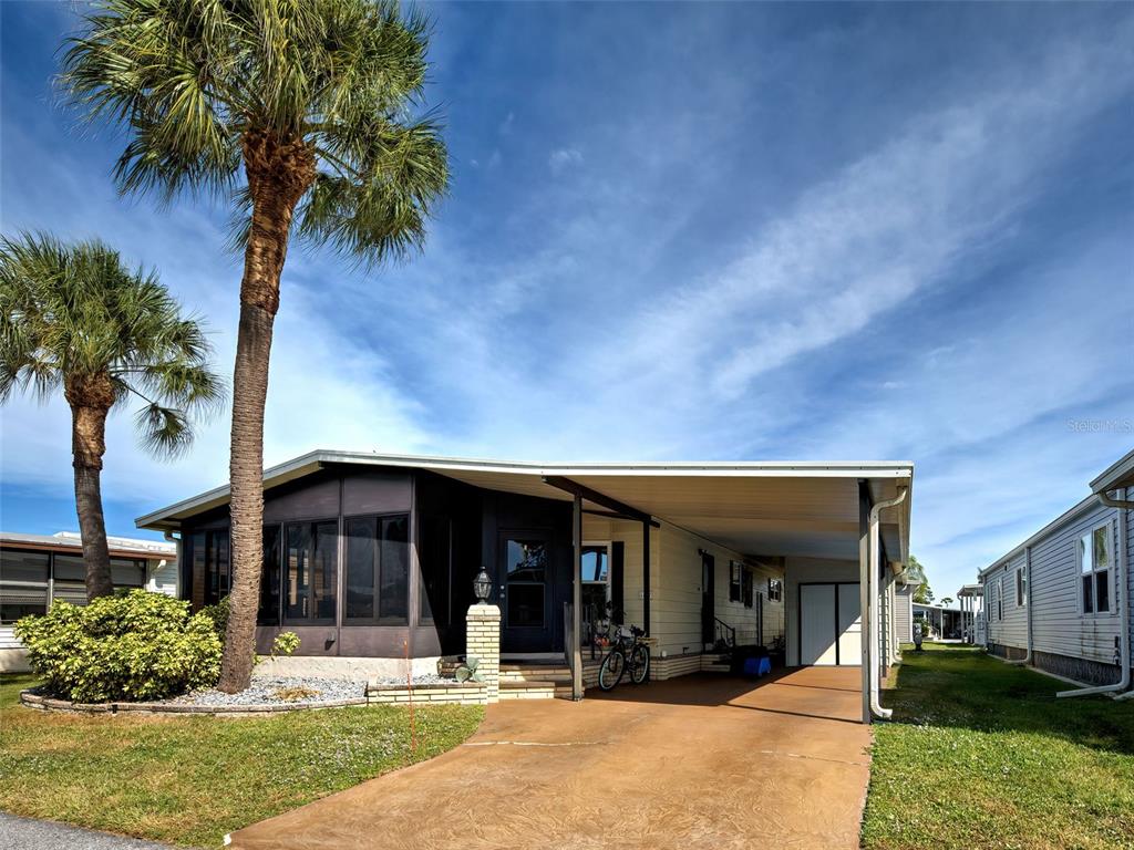 A single-story manufactured home features a screened-in porch, a carport, and two palm trees — 2100 KINGS HIGHWAY UNIT 1067, PORT CHARLOTTE, FL