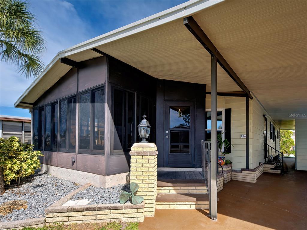 The exterior of a home features a screened-in porch, a brick pillar, and a carport — 2100 KINGS HIGHWAY UNIT 1067, PORT CHARLOTTE, FL