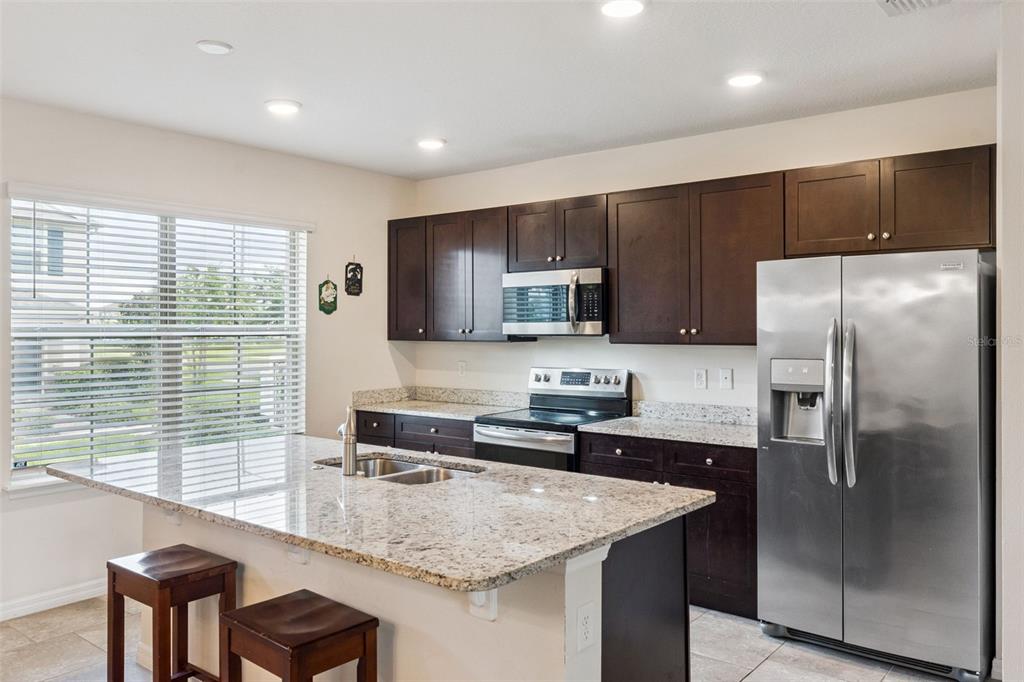 A kitchen features dark wood cabinets, granite countertops, stainless steel appliances, and a central island — 9991 SCHROEDER ALLEY, WINTER GARDEN, FL