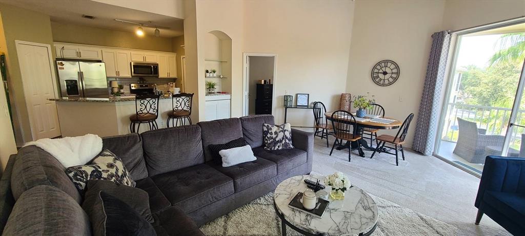 An open-concept living and dining area features a dark sectional sofa, kitchen, and balcony access — 1475 LAKE SHADOW CIRCLE UNIT 6307, MAITLAND, FL