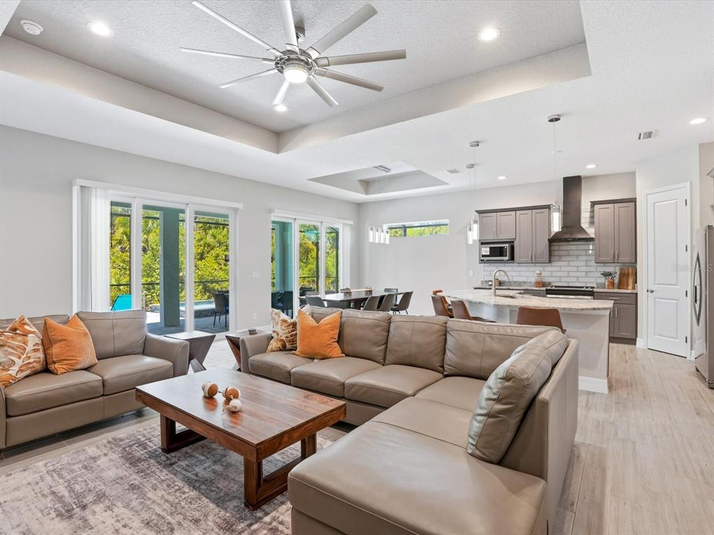 An open-concept living room and kitchen featuring gray leather sofas, wood flooring, and sliding doors — 776 ROTONDA CIRCLE, ROTONDA WEST, FL