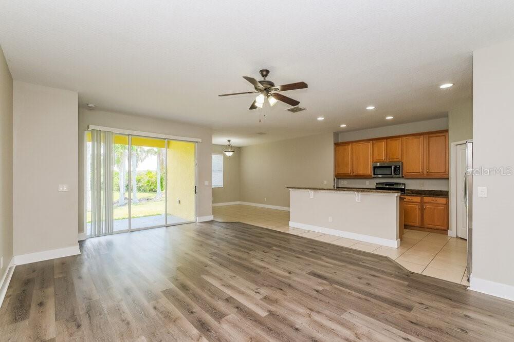 An open-concept living area with wood-look flooring, a kitchen with wood cabinets, and sliding doors — 569 BIMINI BAY BOULEVARD, APOLLO BEACH, FL