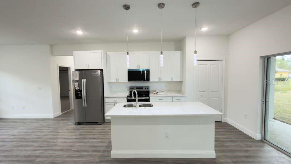 A modern kitchen features white cabinetry, a central island, stainless steel appliances, and wood-look flooring — 2674 W PINTADO DRIVE, CITRUS SPRINGS, FL