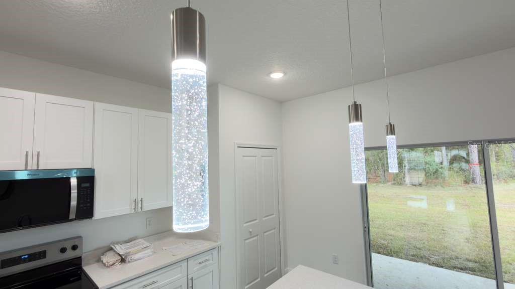 A kitchen features white cabinets, stainless steel appliances, bubble-glass pendant lights, and a sliding glass door — 2674 W PINTADO DRIVE, CITRUS SPRINGS, FL