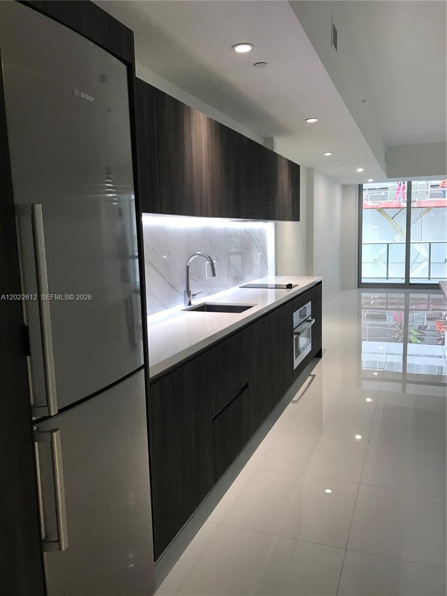 A modern kitchen features dark wood cabinetry, white countertops, a marble backsplash, and stainless appliances — 851 NE 1st Ave # 207, Miami FL 33132, MIAMI, FL