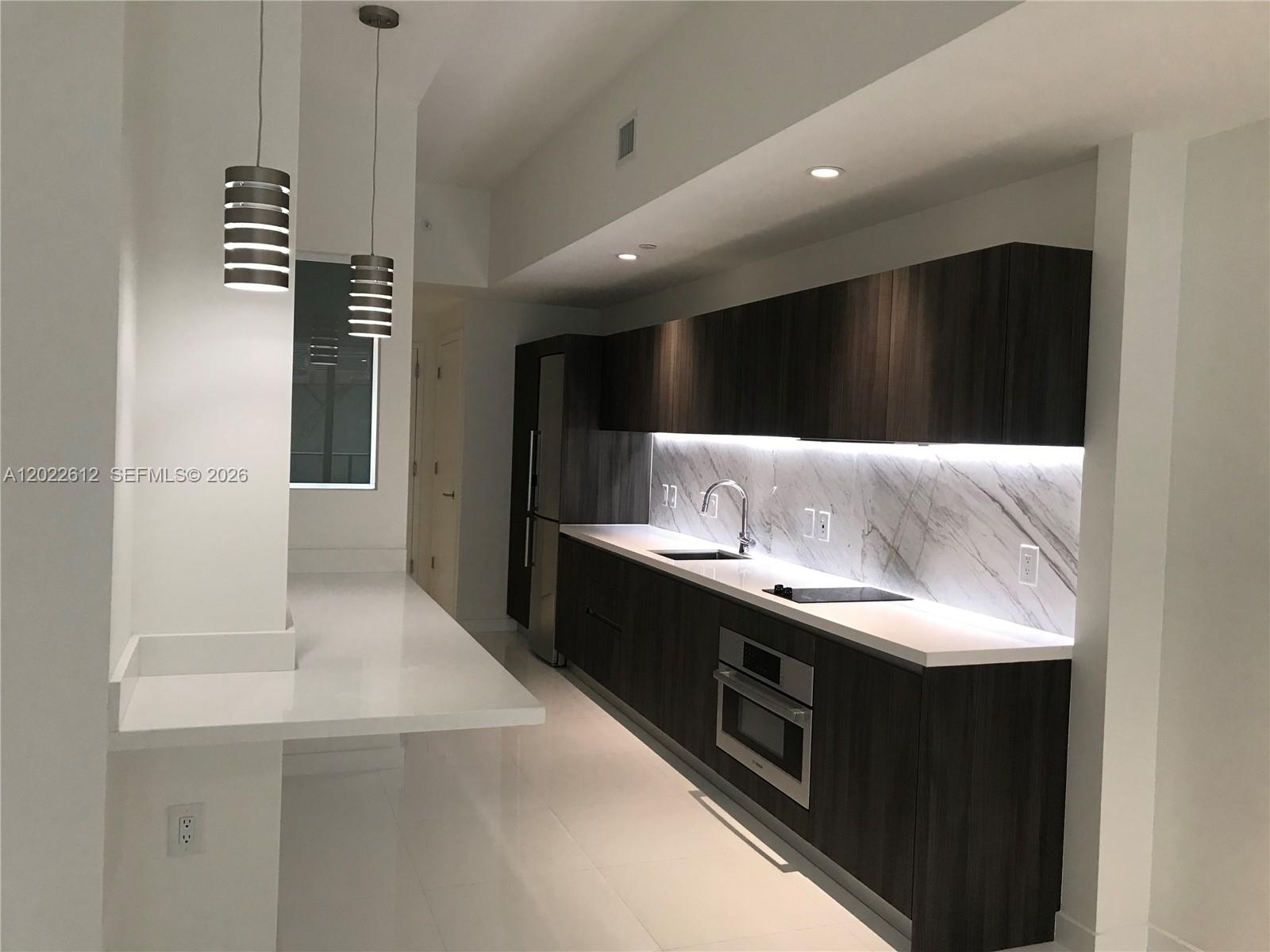 A modern kitchen features dark wood cabinetry, white countertops, and a marble backsplash — 851 NE 1st Ave # 207, Miami FL 33132, MIAMI, FL