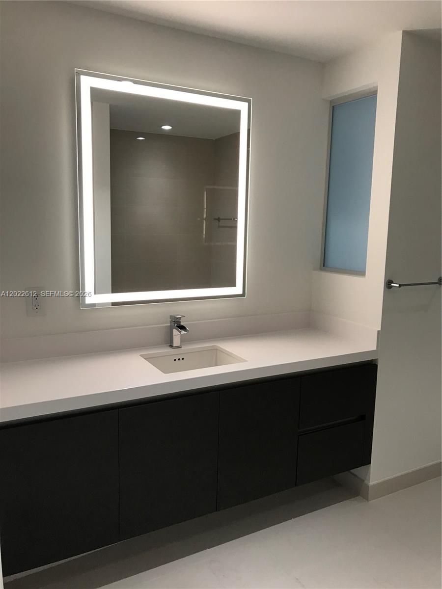 A modern bathroom features a dark vanity, white countertop, and a rectangular LED-lit mirror — 851 NE 1st Ave # 207, Miami FL 33132, MIAMI, FL