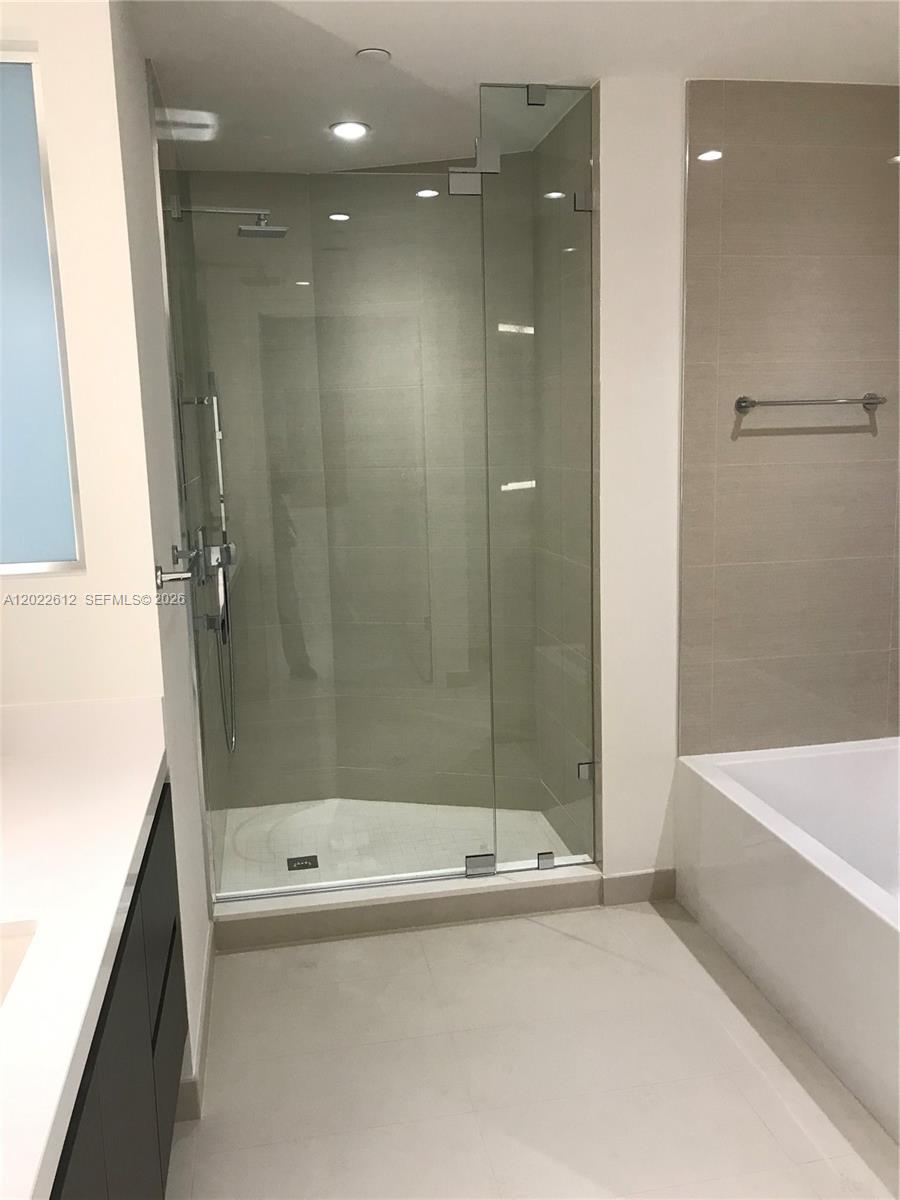 A modern bathroom features a glass-enclosed walk-in shower, a white bathtub, and light-colored tile flooring — 851 NE 1st Ave # 207, Miami FL 33132, MIAMI, FL