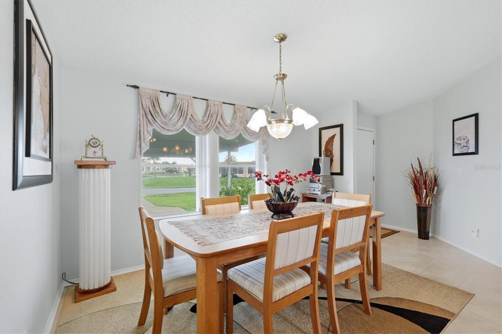 A dining room features a wooden table with six chairs, a chandelier, and a window — 8479 GULL DRIVE, ENGLEWOOD, FL