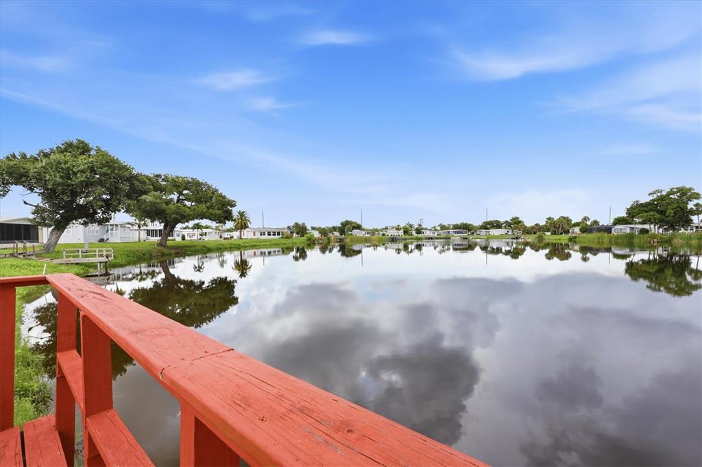 A red wooden railing overlooks a calm pond surrounded by trees and residential homes — 8479 GULL DRIVE, ENGLEWOOD, FL