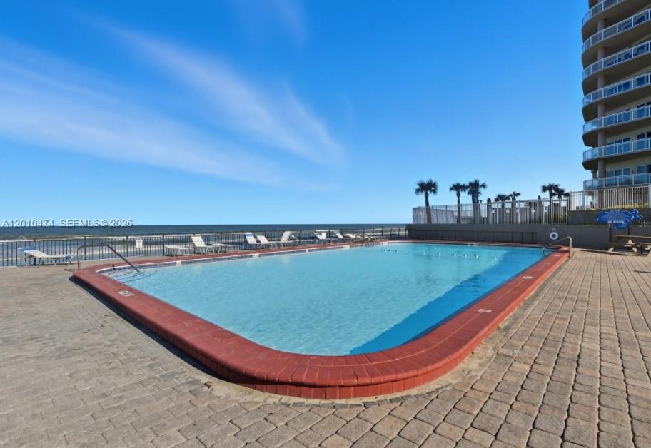 An outdoor swimming pool with a brick border overlooks the ocean next to a building — 1909 S Atlantic Ave # 804, Daytona FL 33118, DAYTONA, FL