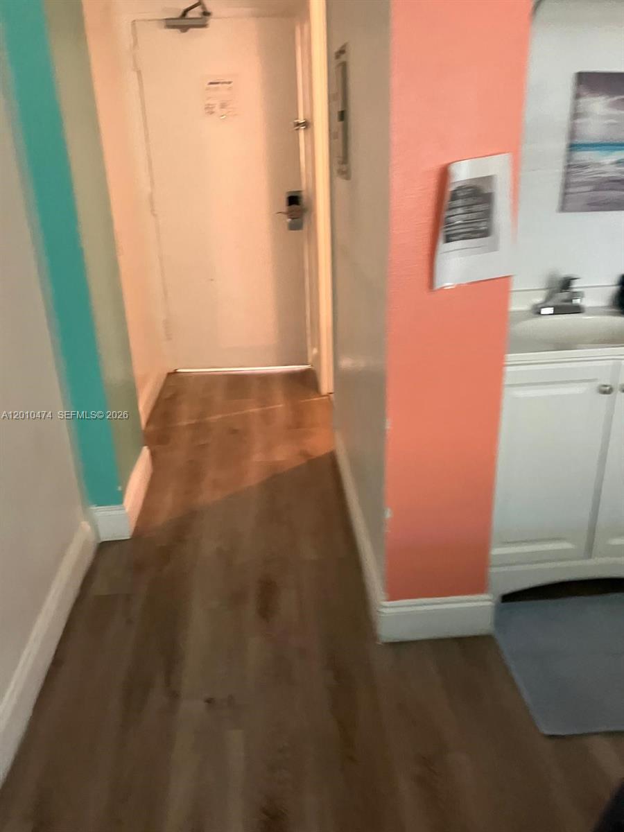 A hallway with wood-look flooring leads to a white door next to a vanity — 1909 S Atlantic Ave # 804, Daytona FL 33118, DAYTONA, FL