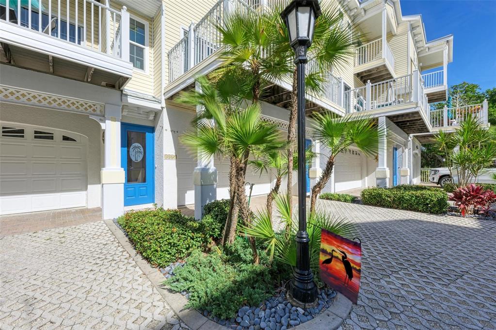 Exterior view of multi-story townhomes with garages, balconies, and a landscaped courtyard with a lamp — 1469 GULF DRIVE N, BRADENTON BEACH, FL