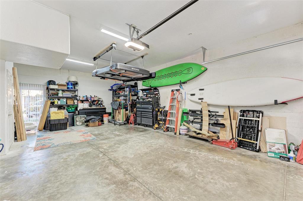 A garage with concrete floors, storage shelving, a ceiling-mounted rooftop tent, and wall-mounted surfboards — 1469 GULF DRIVE N, BRADENTON BEACH, FL