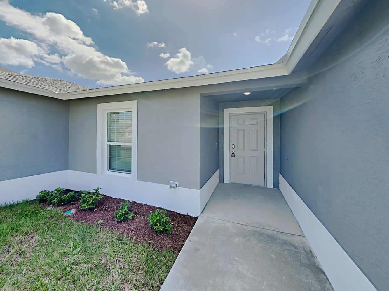 A gray house exterior features a white front door, a single window, and landscaping — PORT ST. LUCIE, FL
