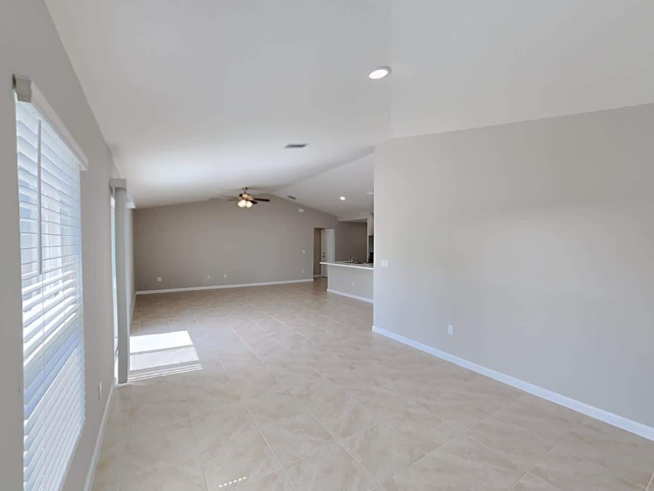 An open-concept living area features light-colored tile flooring, vaulted ceilings, and a kitchen island — PORT ST. LUCIE, FL