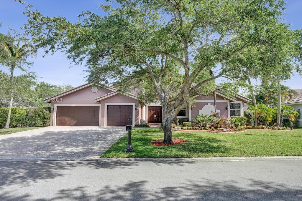 A single-story house with a two-car garage, a paved driveway, and a large front tree — 9921 NW 60th Pl, Parkland FL 33076, PARKLAND, FL