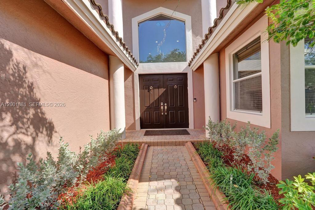 A brick walkway leads to the double front doors of a house with stucco walls — 9921 NW 60th Pl, Parkland FL 33076, PARKLAND, FL
