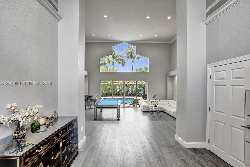 A living room with a pool table, gray wood-look flooring, and a view of a pool — 9921 NW 60th Pl, Parkland FL 33076, PARKLAND, FL