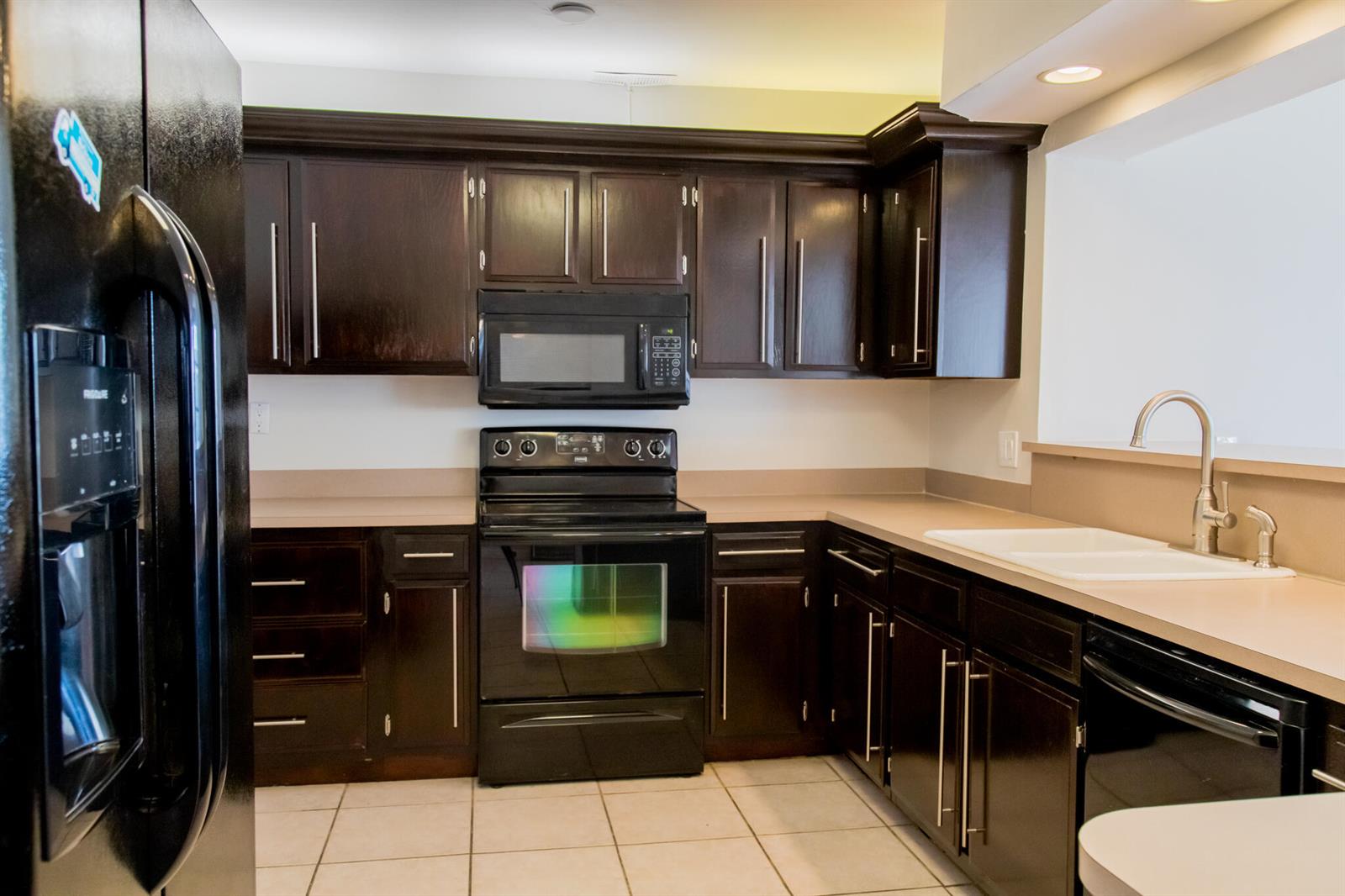 A kitchen featuring dark wood cabinets, black appliances, tan countertops, and a white sink — 130 SW 14th Avenue, Boynton Beach FL 33435, BOYNTON BEACH, FL