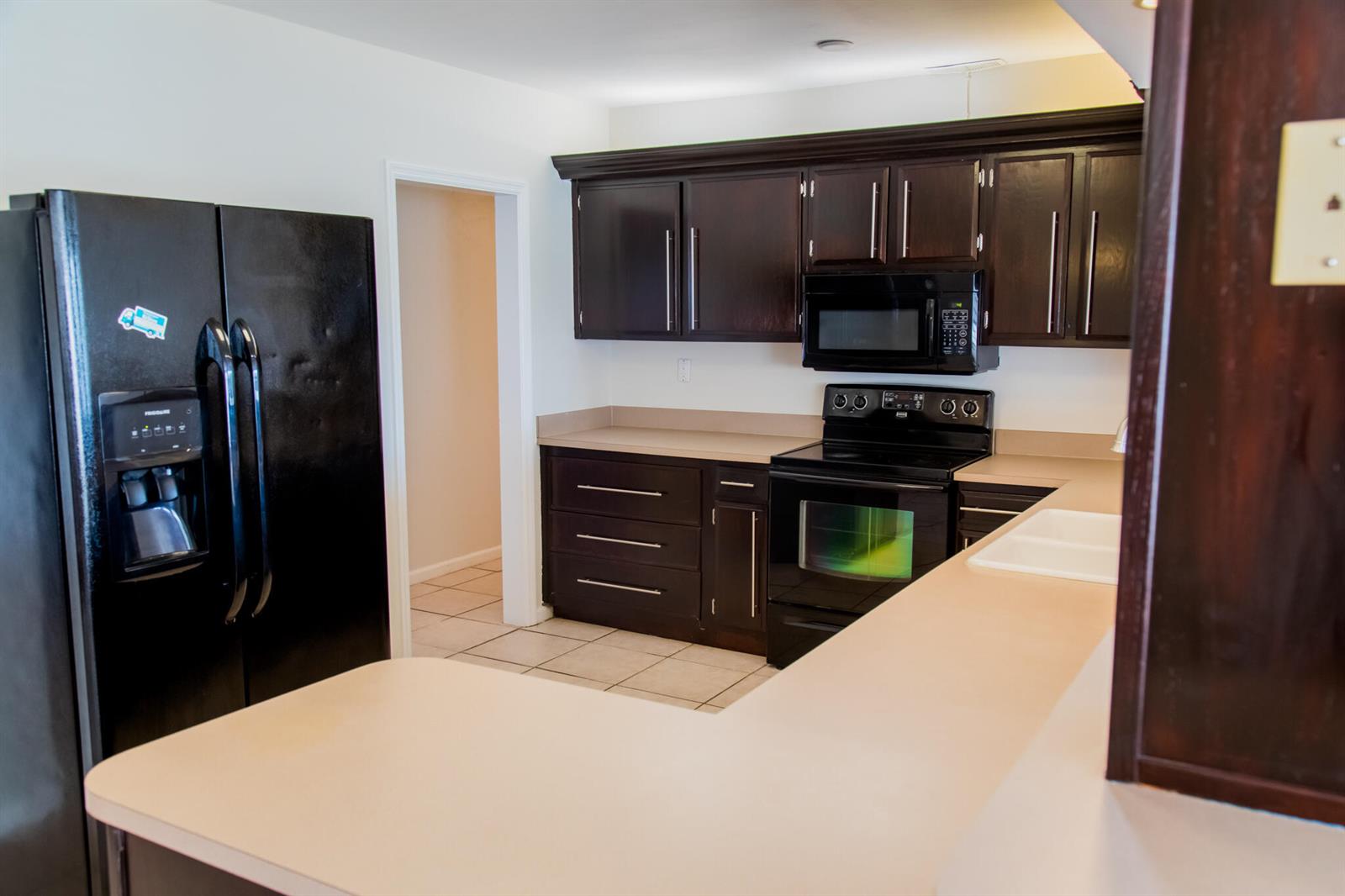 A kitchen features dark wood cabinets, black appliances, and a light-colored countertop — 130 SW 14th Avenue, Boynton Beach FL 33435, BOYNTON BEACH, FL