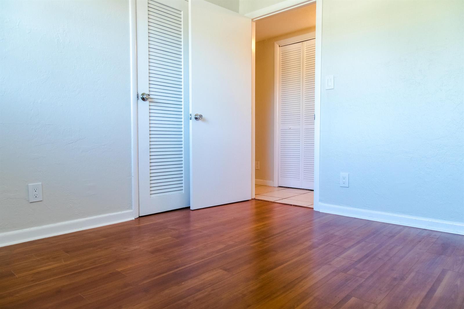 An empty room with wood-look flooring, light blue walls, and two louvered closet doors — 130 SW 14th Avenue, Boynton Beach FL 33435, BOYNTON BEACH, FL