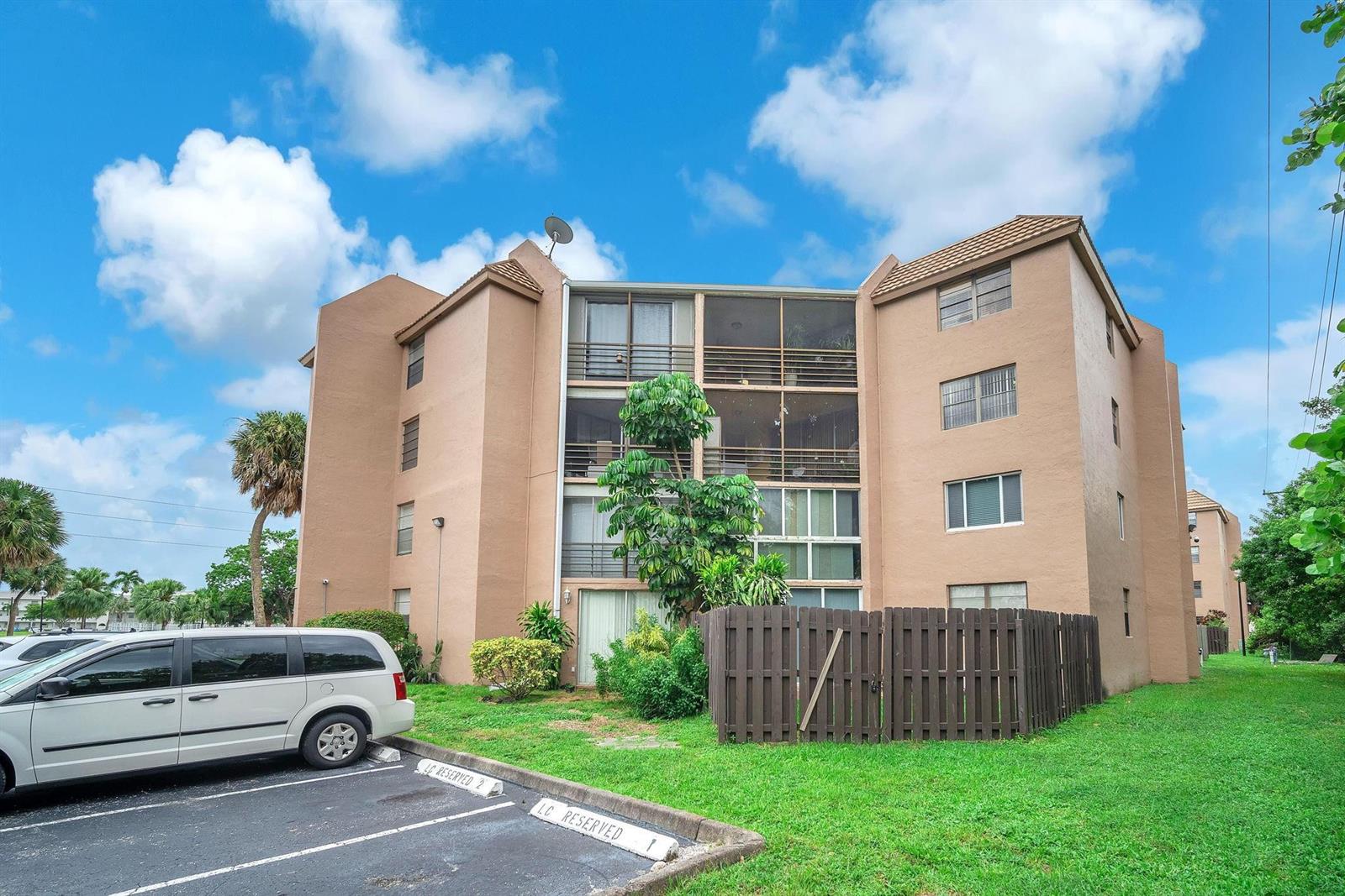 A multi-story tan apartment building with screened balconies stands next to a parking lot — 3100 N Pine Island Road # 306, Sunrise FL 33351, SUNRISE, FL