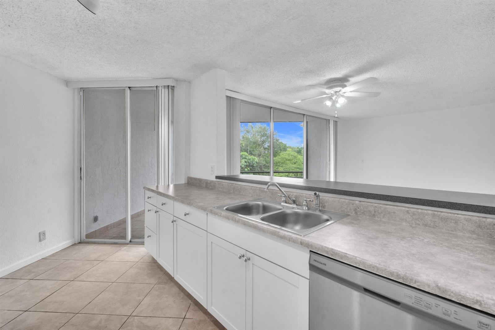 A kitchen with white cabinets, a grey countertop, a double sink, and a sliding door — 3100 N Pine Island Road # 306, Sunrise FL 33351, SUNRISE, FL