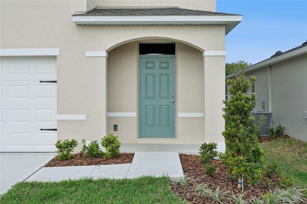 A teal front door is centered under a covered entryway next to a white garage — 2113 WALNUT CREEK DRIVE, KISSIMMEE, FL