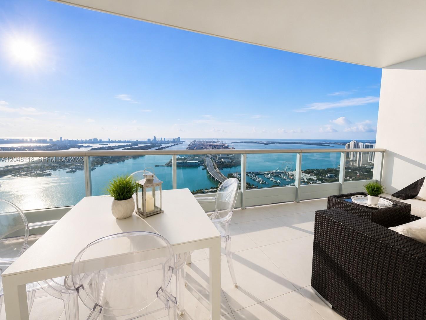 A balcony with outdoor furniture overlooks a bay, a bridge, and a city skyline — 900 Biscayne Blvd # 5505, Miami FL 33132, MIAMI, FL