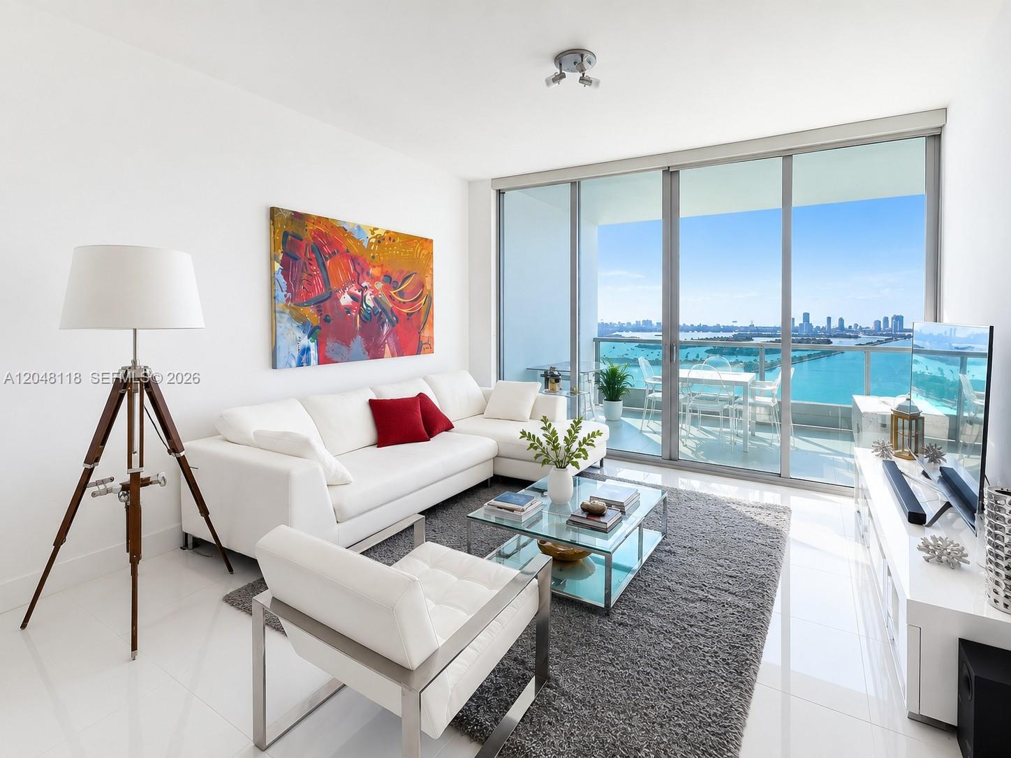 A modern living room features a white sectional sofa, glass coffee table, and balcony view — 900 Biscayne Blvd # 5505, Miami FL 33132, MIAMI, FL