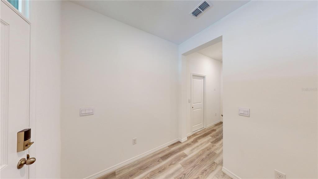 An entryway with white walls, light wood-look flooring, and a door leading to a hallway — 17280 BIGLEAF MAHOGANY LANE, LAND O LAKES, FL