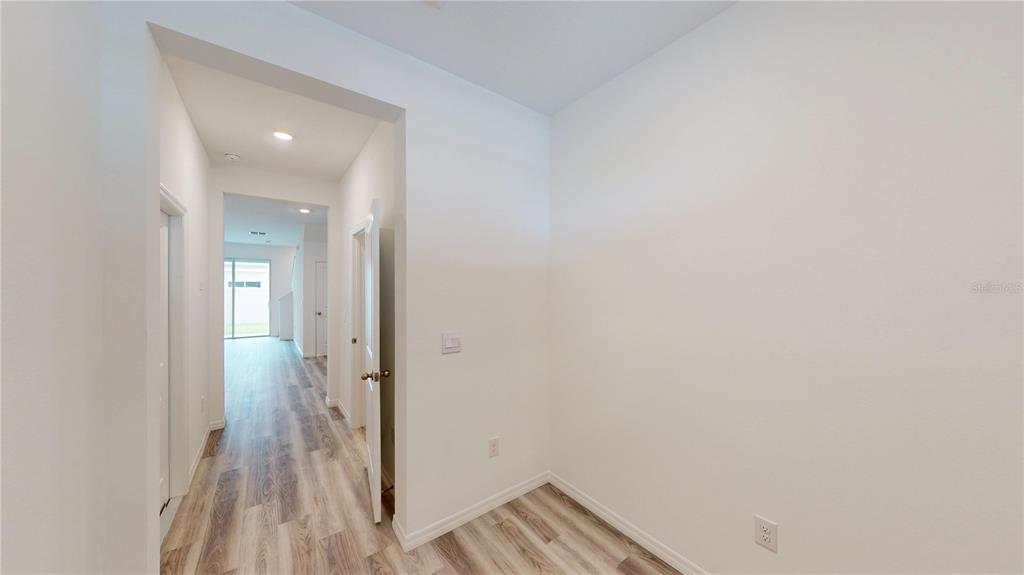 A hallway with light wood-look flooring leads toward a bright room with a glass door — 17280 BIGLEAF MAHOGANY LANE, LAND O LAKES, FL