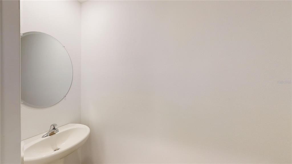 A small bathroom features a white pedestal sink and a round frameless wall mirror — 17280 BIGLEAF MAHOGANY LANE, LAND O LAKES, FL