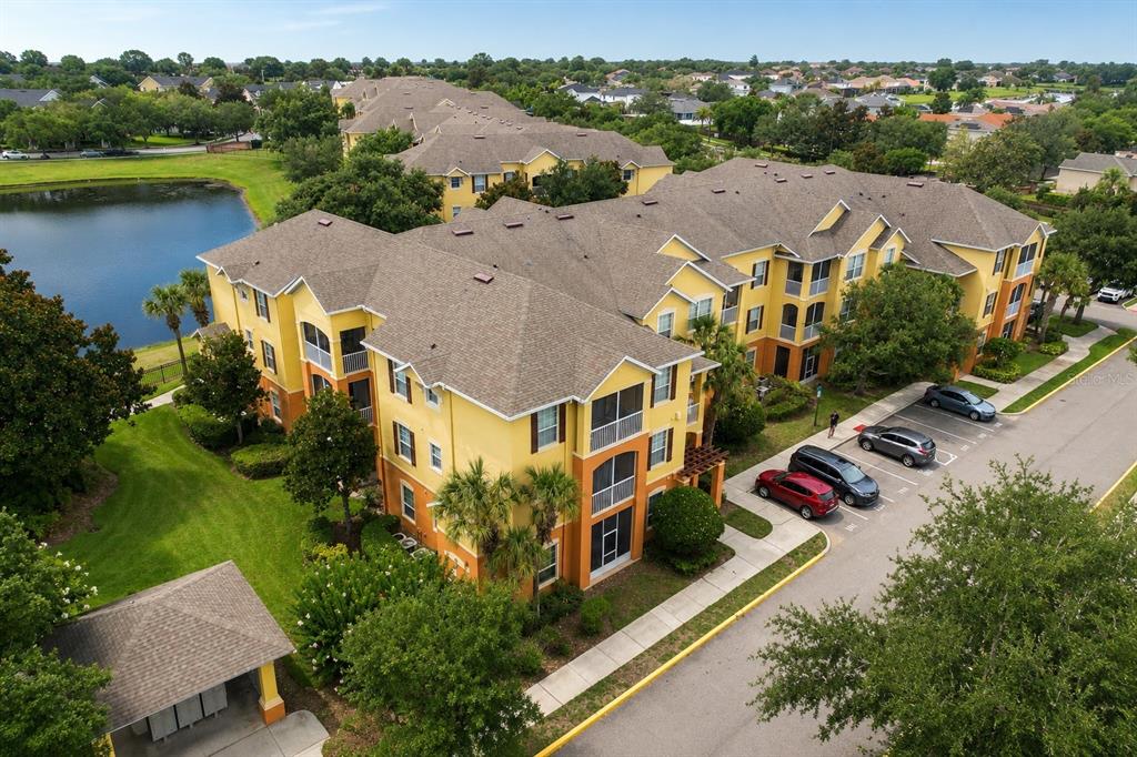 An aerial view of a yellow multi-story apartment building next to a lake and parking — 6240 CONTESSA DRIVE UNIT 204, ORLANDO, FL