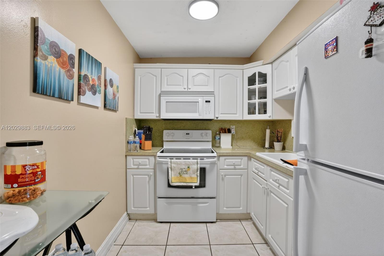A small kitchen features white cabinets, white appliances, beige walls, and light-colored tile flooring — 11790 SW 18th St # 3, Miami FL 33175, MIAMI, FL