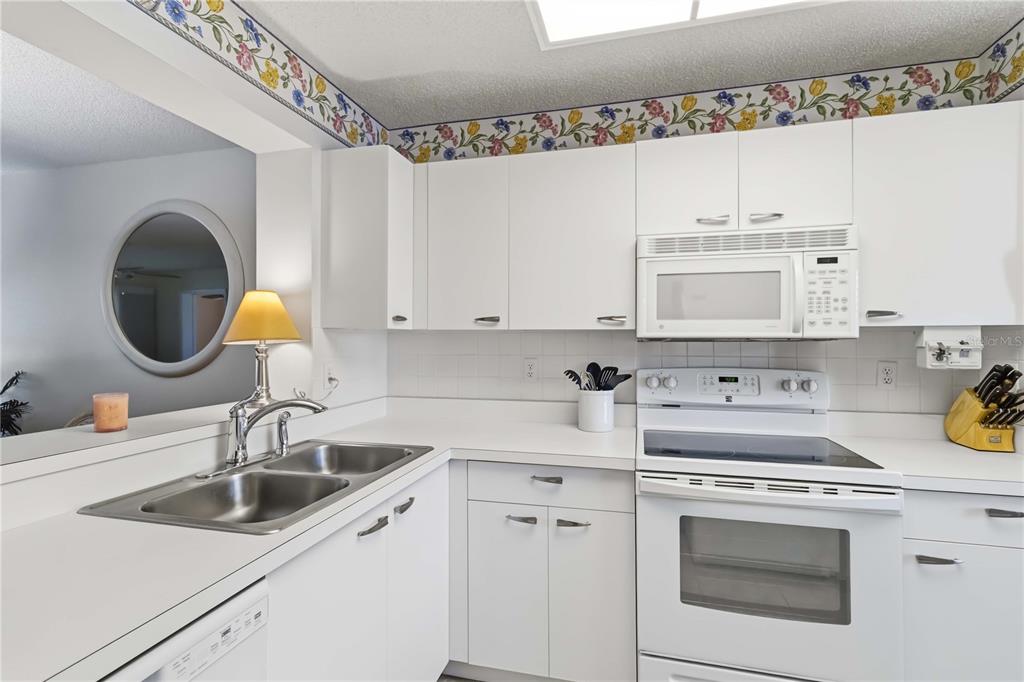 A kitchen with white cabinets, white appliances, a double sink, and floral wallpaper border — 3950 IRONWOOD CIRCLE UNIT 205, BRADENTON, FL