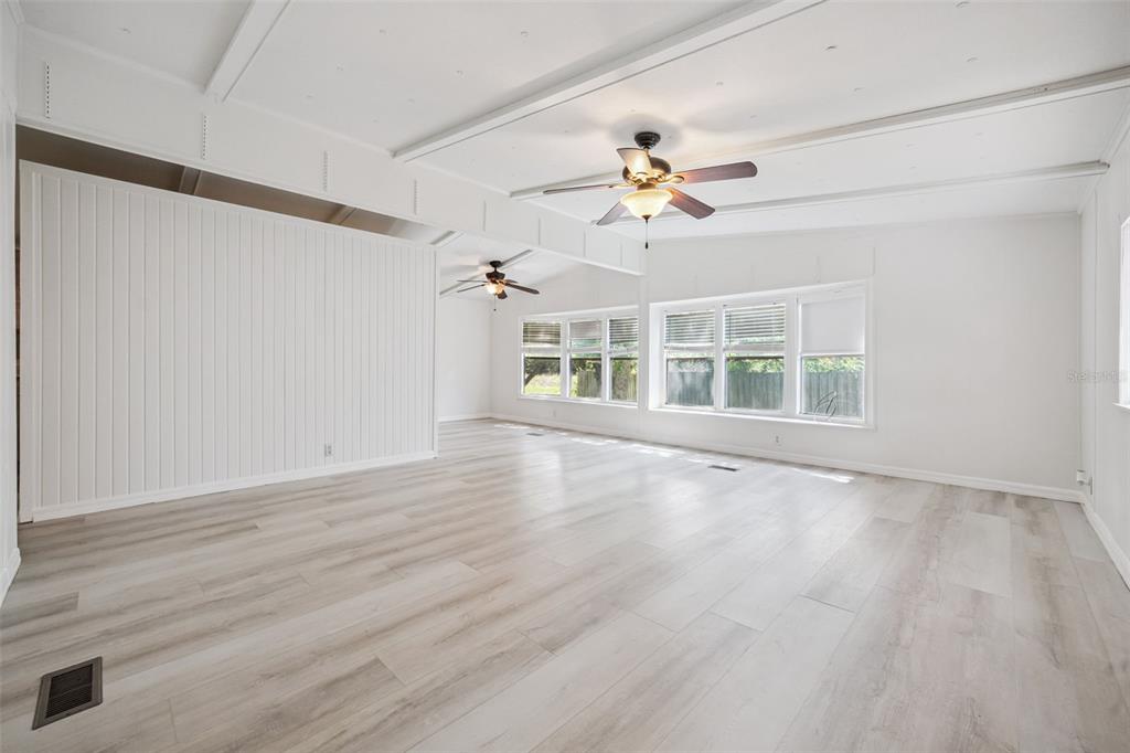 A spacious, empty room features light wood-look flooring, white paneled walls, and two ceiling fans — 16802 SUGAR BERRY LANE, MONTVERDE, FL