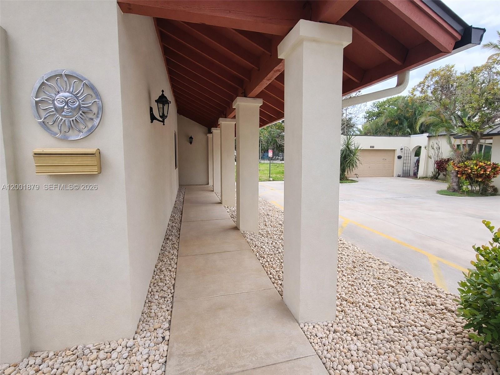 A covered concrete walkway features white pillars and a sun-themed wall decoration — 5524 Constant Spring Ter # 213, Lauderhill FL 33319, LAUDERHILL, FL