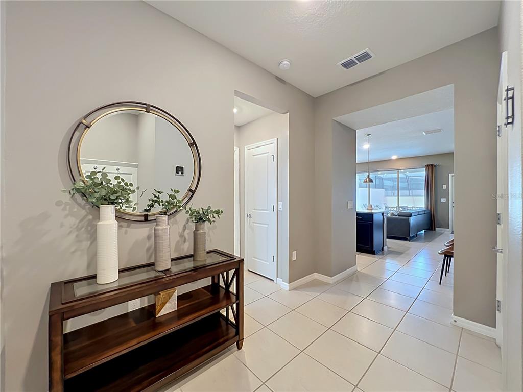 A foyer features a dark wood console table, a round mirror, and tile flooring — 616 JASMINE LANE, DAVENPORT, FL