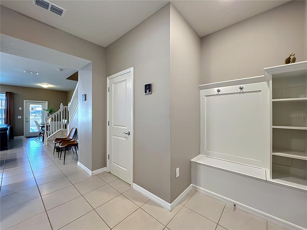 A tiled entryway features a white built-in mudroom bench, a closed door, and a staircase — 616 JASMINE LANE, DAVENPORT, FL