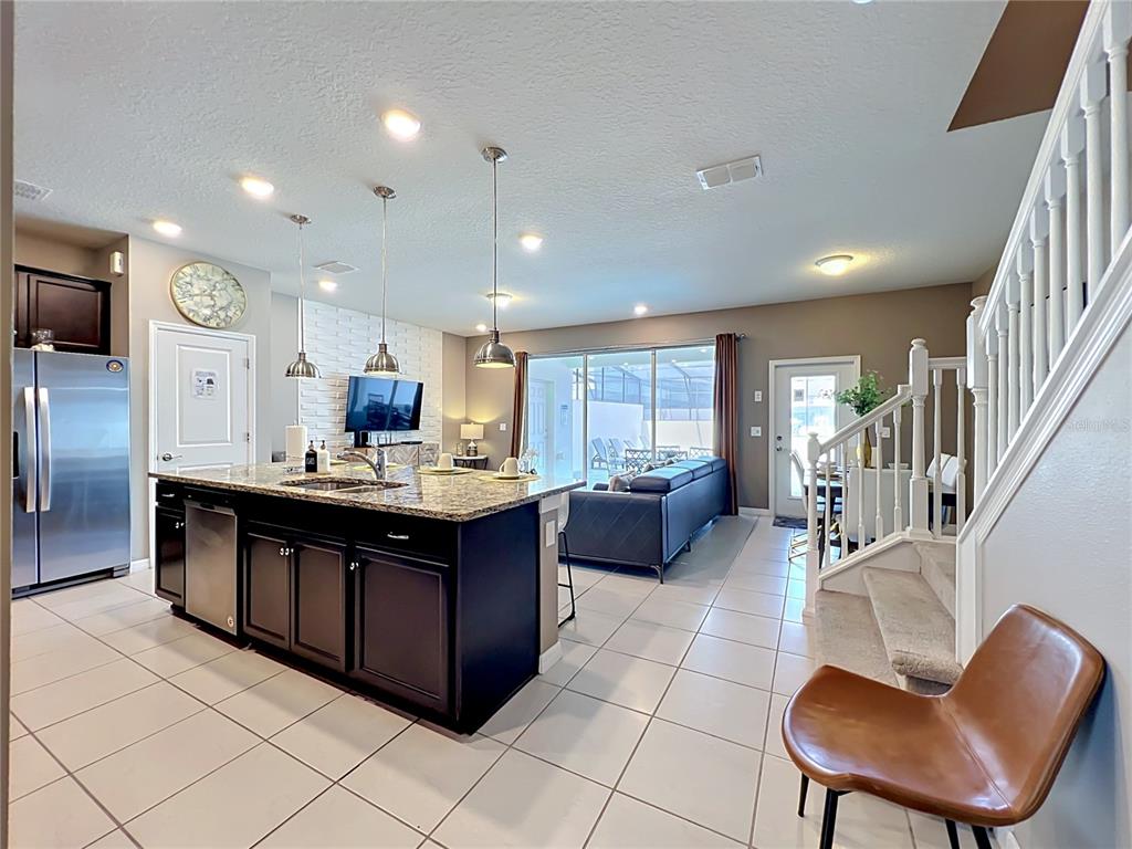 A kitchen with a dark island and granite countertops opens into a living area — 616 JASMINE LANE, DAVENPORT, FL