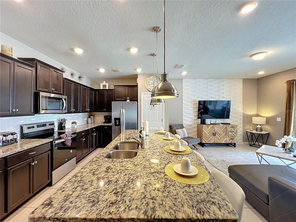 A kitchen with dark cabinets and granite countertops features an island overlooking a living area — 616 JASMINE LANE, DAVENPORT, FL