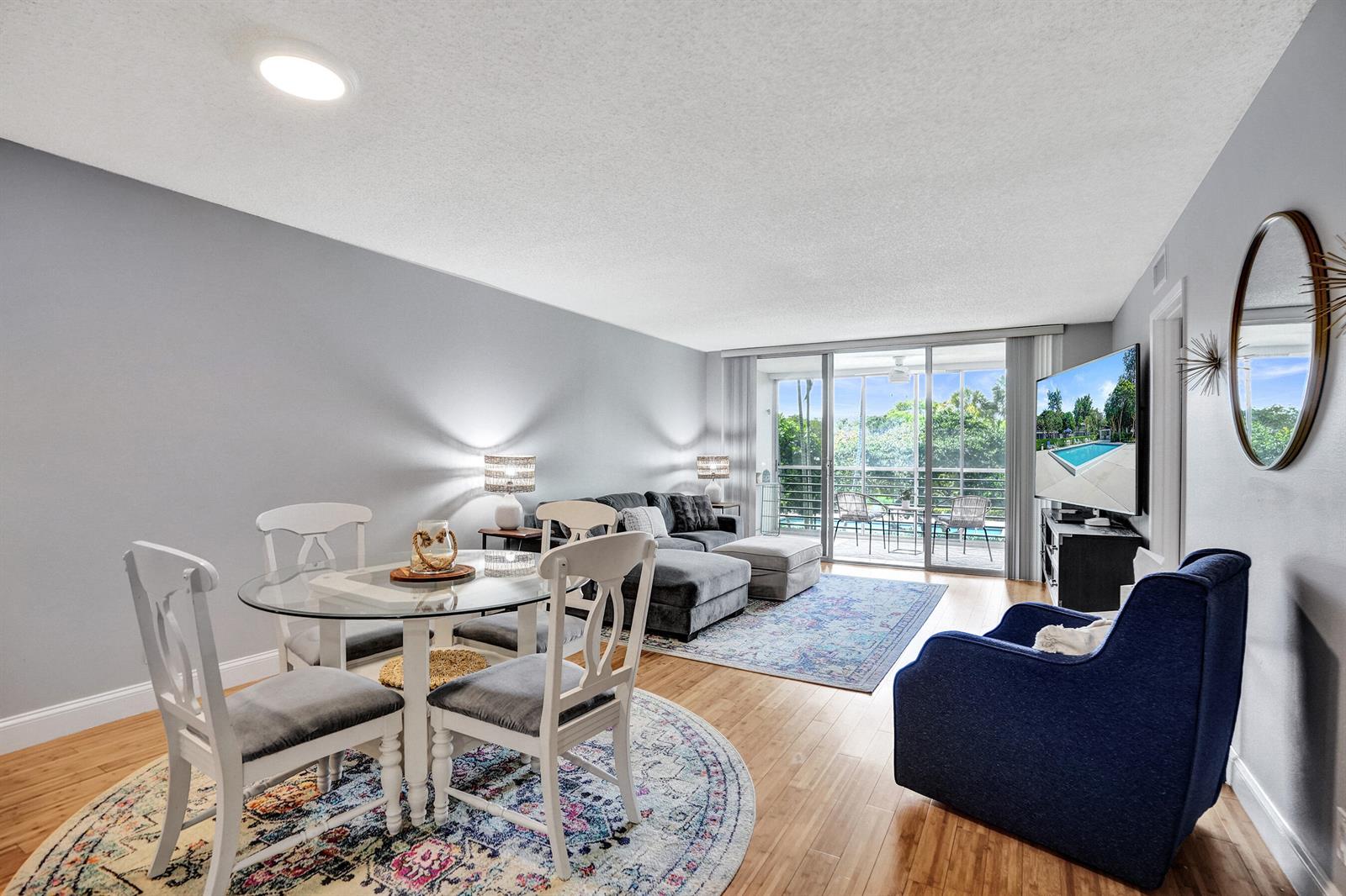 A living and dining area features a glass table, gray sectional, blue armchair, and balcony — 4200 Oaks Terrace # 203, Pompano Beach FL 33069, POMPANO BEACH, FL